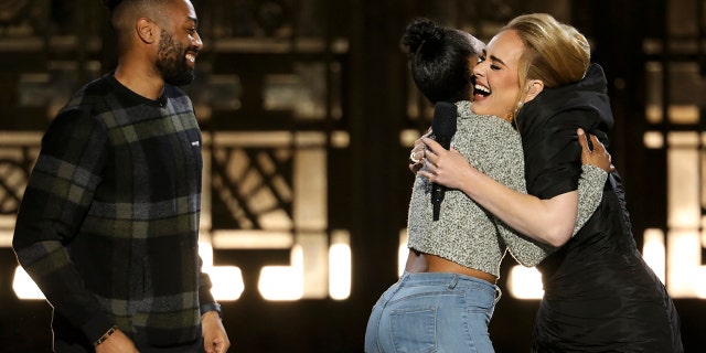 Quentin Brunson, left, looks on as his fiancée, Ashleigh Mann, hugs Adele after saying ‘yes' to his marriage proposal at the Grammy winner's primetime performance.
