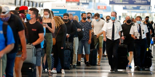 FILE - Two airplane pilots pass by a line of passengers while waiting at a security check-in line at O'Hare International Airport in Chicago, ahead of Fourth of July weekend, July 1, 2021.  (AP Photo/Shafkat Anowar, File) 