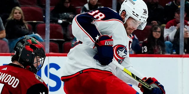 Columbus Blue Jackets center Boone Jenner (38) has the puck hit his skate in front of Arizona Coyotes goalie Scott Wedgewood (31) during the second period of an NHL hockey game Thursday, Nov. 18, 2021, in Glendale, Ariz.