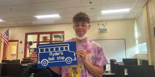 Student Mason Heald holding the sign that he designed and made for Ryder Killam's bus stop. 