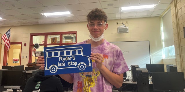 Student Mason Heald holding the sign that he designed and made for Ryder Killam's bus stop.