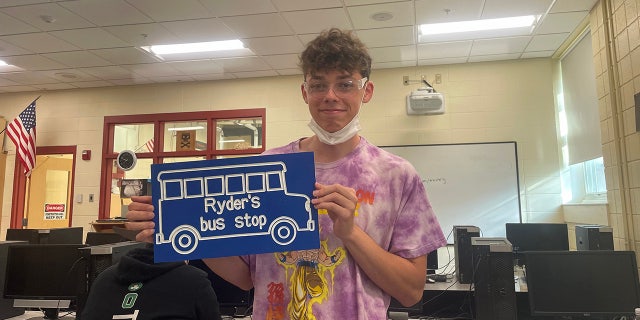 Student Mason Heald holding the sign that he designed and made for Ryder Killam's bus stop. 