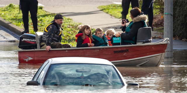 Um voluntário dirigindo um barco resgata uma mulher e crianças presas pela enchente devido à enchente, enquanto o veículo de outra pessoa está submerso perto deles em Abbotsford, British Columbia, terça-feira, 16 de novembro de 2021.