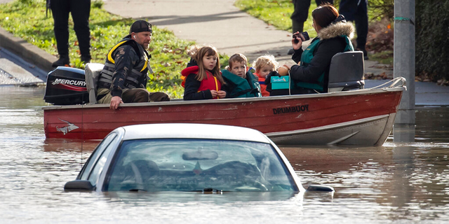 Um voluntário dirigindo um barco resgata uma mulher e crianças presas pela enchente devido à enchente, enquanto o veículo de outra pessoa está submerso perto deles em Abbotsford, British Columbia, terça-feira, 16 de novembro de 2021.