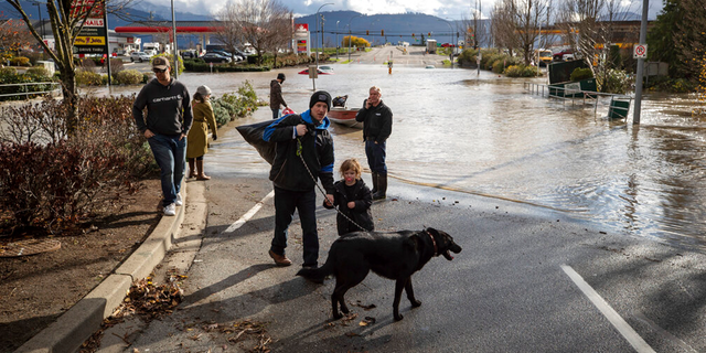 رجل وطفل صغير وكلب تم إنقاذهم من قبل متطوع من قارب بعد أن تقطعت بهم السبل بسبب ارتفاع منسوب المياه بسبب فيضان سير على مرتفعات في أبوتسفورد ، كولومبيا البريطانية يوم الثلاثاء 16 نوفمبر 2021.