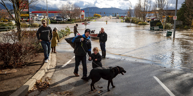 Um homem, uma criança e um cachorro resgatados por um voluntário em um barco após ficarem presos na enchente devido a uma enchente, caminham em um terreno mais alto, em Abbotsford, British Columbia, na terça-feira, 16 de novembro de 2021.