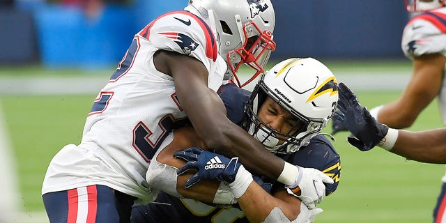 Austin Ekeler of the Los Angeles Chargers runs with the ball while being tackled by Devin McCourty of the New England Patriots in the fourth quarter at SoFi Stadium on Oct. 31, 2021, in Inglewood, California.