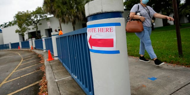A woman walks past a sign directing voters to a polling place, at Sea Castle Elementary School in Miramar, Fla., on Election Day, Tuesday, Nov. 2, 2021. Eleven Democrats are on the ballot in Tuesday's primary special election for the seat of Democratic Rep. Alcee Hastings, who died in April after suffering from pancreatic cancer.(AP Photo/Rebecca Blackwell)