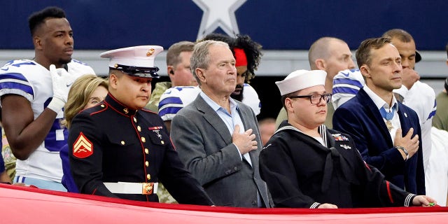 El ex presidente George W. Bush.  Bush se encuentra entre los miembros de las Fuerzas Armadas de los Estados Unidos mientras suena el himno nacional antes de la primera mitad de un partido de fútbol americano de la NFL.