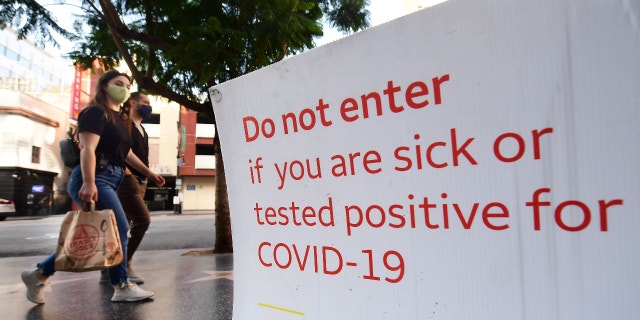 Pedestrians wearing facemasks walk past a sign posting Covid-19 requirements in front of a store in Hollywood, California on November 2, 2021. (Photo by Frederic J. BROWN / AFP) (Photo by FREDERIC J. BROWN/AFP via Getty Images)