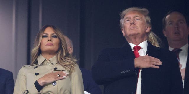 ATLANTA, GEORGIA - OCTOBER 30:  Former first lady and president of the United States Melania and Donald Trump stand for the national anthem prior to Game Four of the World Series between the Houston Astros and the Atlanta Braves Truist Park on October 30, 2021 in Atlanta, Georgia. (Photo by Elsa/Getty Images)