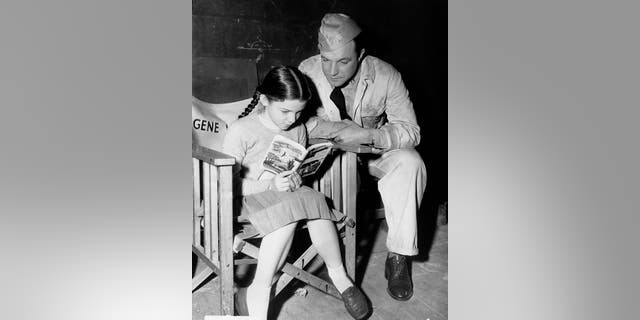 Gene Kelly is seen here listening to his daughter Kerry reading aloud from 'Worzel Gummidge' by Barbara Euphan Todd on the set of the MGM film 'Crest of the Wave' in London, circa 1953. The film was based on the play 'Seagulls Over Sorrento' by Hugh Hastings. 
