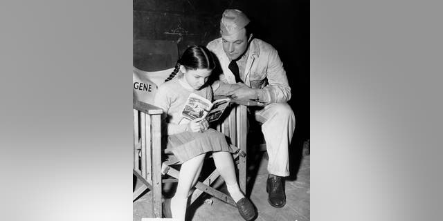 Gene Kelly is seen here listening to his daughter Kerry reading aloud from 'Worzel Gummidge' by Barbara Euphan Todd on the set of the MGM film 'Crest of the Wave' in London, circa 1953. The film was based on the play 'Seagulls Over Sorrento' by Hugh Hastings.