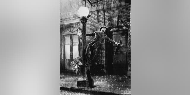 Gene Kelly swings from a lamp post in a still from the film, 'Singin' In The Rain' directed by Kelly and Stanley Donen, 1952.