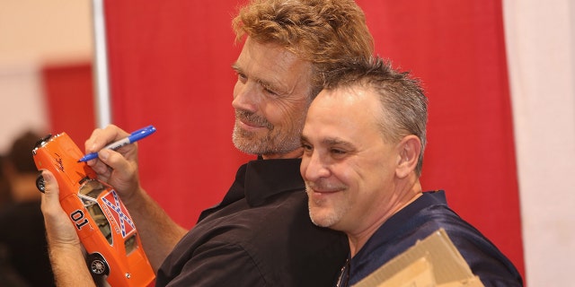 John Schneider autographs a miniature "General Lee" and poses with a fan at the Motor City Comic Con at Suburban Collection Showplace on May 16, 2015, in Novi, Michigan.