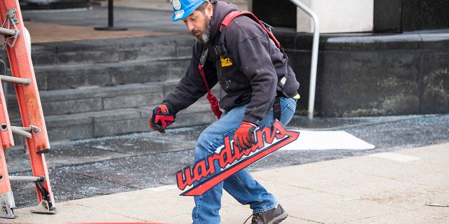 A worker from the Brilliant Electric Sign Company holds a broken piece of the Cleveland Guardians team store sign in Cleveland, Friday, Nov. 19, 2021, in Cleveland. The sign was being installed and fell off the building.