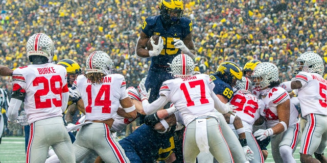 Michigan running back Hassan Haskins (25) leaps over Ohio State defenders for a touchdown in the second quarter of an NCAA college football game in Ann Arbor, 自分。, 土曜日, 11月. 27, 2021.
