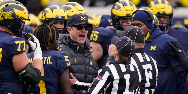 Referees talk to Michigan head coach Jim Harbaugh during the second half of an NCAA college football game against Ohio State, Saturday, Nov. 27, 2021, in Ann Arbor, Mich.