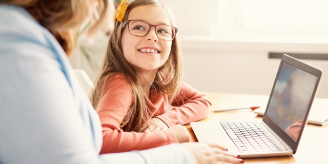 A mother and daughter sit at home with a laptop 