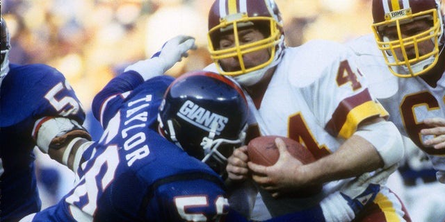 Linebacker Lawrence Taylor of the New York Giants has running back John Riggins of the Washington Redskins in his grasp circa 1985 during an NFL football game at RFK Stadium in Washington, D.C.