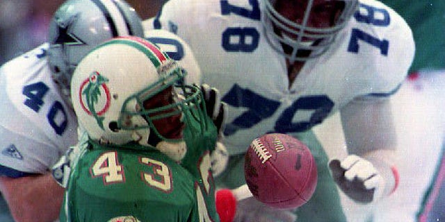 Miami Dolphins running back Terry Kirby (43) loses the ball while being brought down by the Dallas Cowboys' Brock Marion (31), Leon Lett (78) and Bill Bates (40) during first quarter action Nov. 25, 1993 in Texas. The Cowboys recovered the ball.