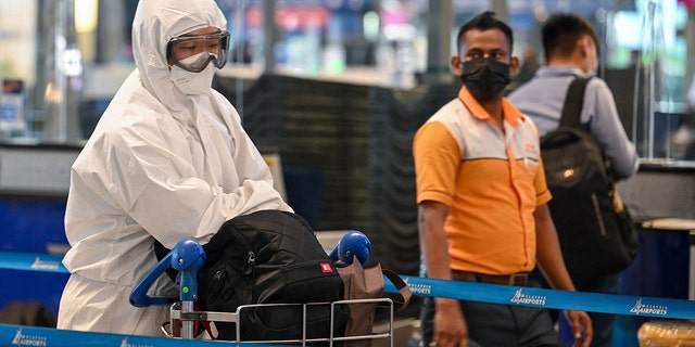 A passenger wearing personal protective equipment queues to check-in for a flight at the Kuala Lumpur International Airport on Nov. 29, 2021, as countries across the globe shut borders and renewed travel curbs in response to the spread of a new, heavily mutated COVID-19 coronavirus variation. (Photo by Mohd RASFAN / AFP)Â 
