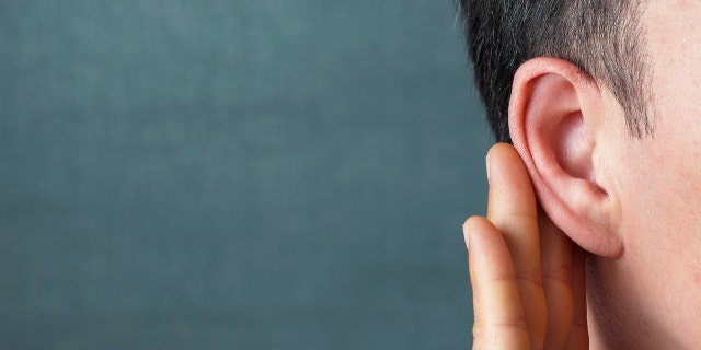 The man listens carefully with her palm to her ear, close-up