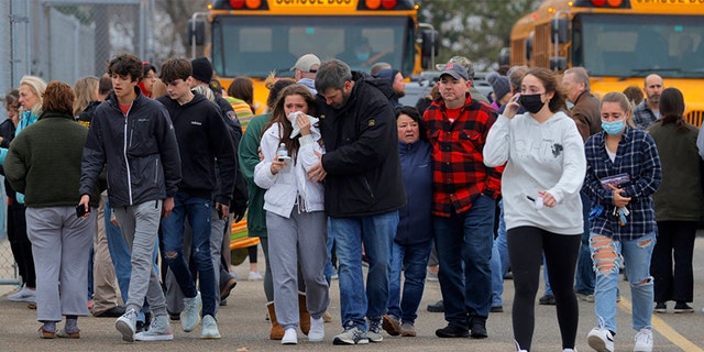 Parents walk away with their kids from the Meijer's parking lot in Oxford where many students gathered following an active shooter situation at Oxford High School in Oxford on November 30, 2021.