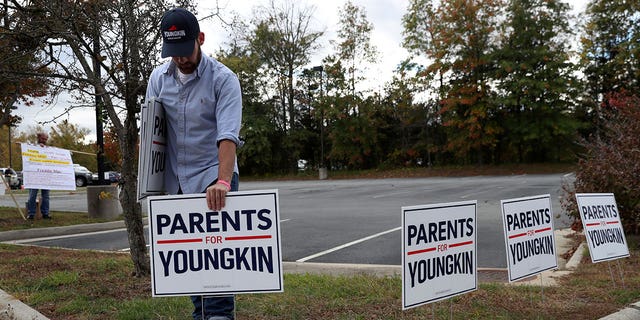 Tristan Thorgersen puts pro-Youngkin signs up as people gather to protest different issues including the board’s handling of a sexual assault that happened in a school bathroom in May, vaccine mandates and critical race theory during a Loudoun County School Board meeting in Ashburn, Virginia.