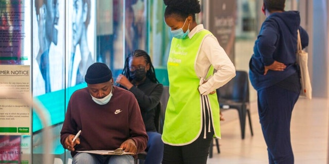 Las personas se reúnen para vacunarse en el centro comercial de Johannesburgo el viernes 26 de noviembre de 2021.  Se ha descubierto una nueva versión del coronavirus en Sudáfrica, que según los científicos es preocupante debido a la rápida propagación de una gran cantidad de mutaciones en los jóvenes.  personas en Gauteng, el estado más poblado del país.  (Foto AP / Denis Farrell)