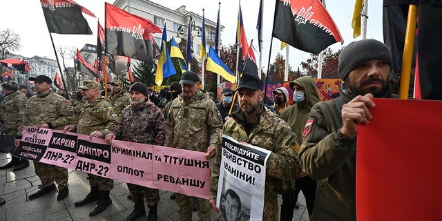 Dalībnieki karā ar Krievijas atbalstītajiem separātistiem Ukrainas austrumos, galēji labējās, galēji labējās kustības aktīvisti, mītiņa laikā nēsā plakātus un karogus. "Izbeidziet rāpojošo okupāciju!" Ārpus Ukrainas prezidenta Volodimira Zeļenska biroja Kijevā 2021. gada 4. novembrī. 