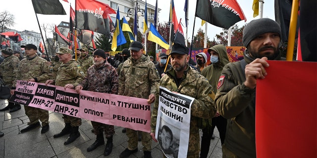 Dalībnieki karā ar Krievijas atbalstītajiem separātistiem Ukrainas austrumos, galēji labējās, galēji labējās kustības aktīvisti, mītiņa laikā nēsā plakātus un karogus. "Izbeidziet rāpojošo okupāciju!" Ārpus Ukrainas prezidenta Volodimira Zeļenska biroja Kijevā 2021. gada 4. novembrī. 