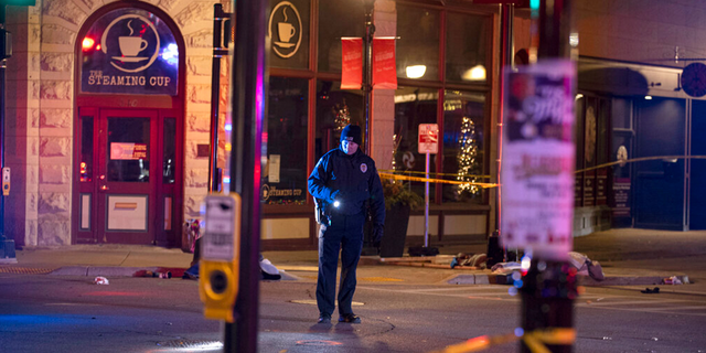 A police officer uses a flashlight while looking for evidence in downtown Waukesha, Wis., after an SUV sped through a barricade and slammed into a Christmas parade, injuring multiple people Sunday, Nov. 21, 2021.