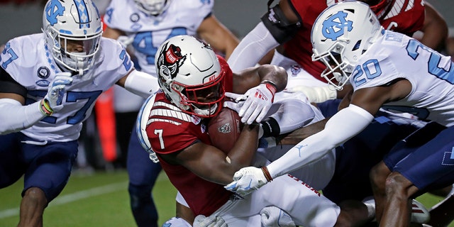 North Carolina State running back Zonovan Knight (7) gets tackled by North Carolina defensive back Giovanni Biggers (27) and defensive back Tony Grimes (20) during the first half of an NCAA college football game Friday, Nov. 26, 2021, in Raleigh, North Carolina.