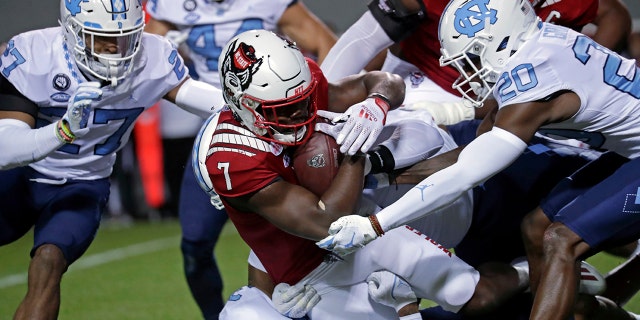 North Carolina State running back Zonovan Knight (7) gets tackled by North Carolina defensive back Giovanni Biggers (27) and defensive back Tony Grimes (20) during the first half of an NCAA college football game Friday, Nov. 26, 2021, in Raleigh, North Carolina.