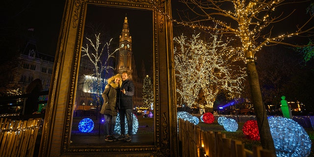 A couple poses for a photograph backdropped by the building of the city hall at a Christmas market in Vienna, Austria, Sunday, Nov. 21, 2021. 