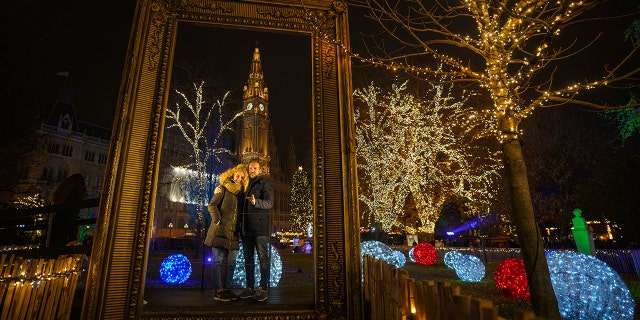 A couple poses for a photograph backdropped by the building of the city hall at a Christmas market in Vienna, Austria, Sunday, Nov. 21, 2021. 