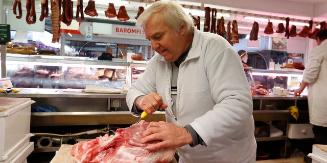 Vendor Misi Kovacs prepares the meat to sell in a food market in Budapest, Hungary, Nov. 20, 2021.