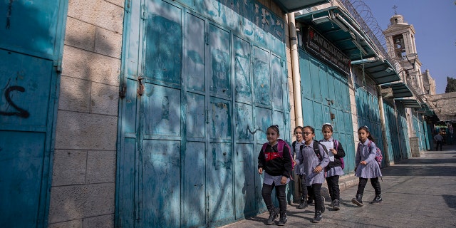 Des enfants palestiniens passent devant des boutiques de souvenirs fermées sur le marché aux touristes adjacent à l'église de la Nativité, dans la ville cisjordanienne de Bethléem, le mardi 16 novembre 2021.