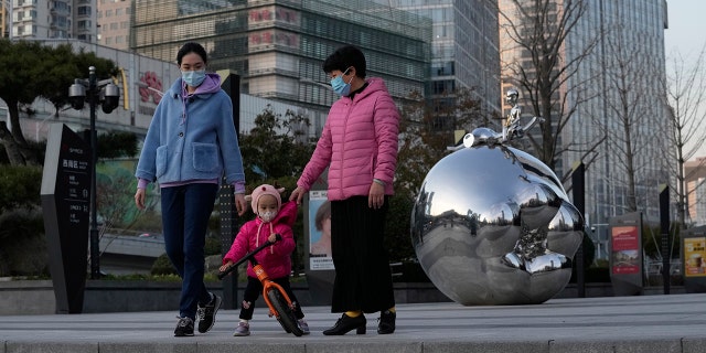 Bewohner, die am Samstag Masken tragen, kommen an einem Kunstwerk vor einem Einkaufszentrum in Peking, China, vorbei.