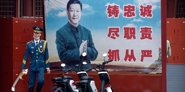 A Chinese honor guard member walks past a poster of Chinese leader Xi Jinping near the entrance to the Forbidden City in Beijing on Sept. 18, 2021.  President Xi has been absent from the Group of 20 summit in Rome and global climate talks in Scotland, drawing criticism from U.S. President Biden and questions about China’s commitment to reducing greenhouse gas emissions.  