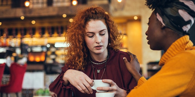 A young woman is talking with a female friend about her problem in a cafe. The friend is supportive and understanding.