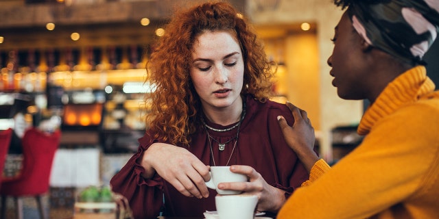 A young woman is talking with a female friend about her problem in a cafe. The friend is supportive and understanding.