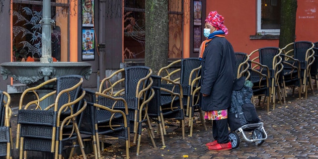 A woman wears a face mask to protect herself against the coronavirus as she passes by an empty terrace in the Marrolles quarter in Brussels, Belgium, Nov. 17, 2021.