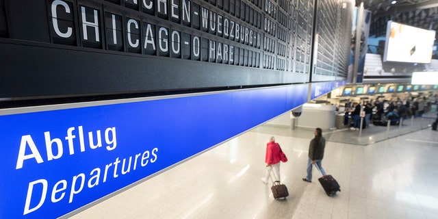 A flight to Chicago O'Hare in the USA is displayed on a board at Frankfurt airport under which passengers with suitcases walk along on Monday. 