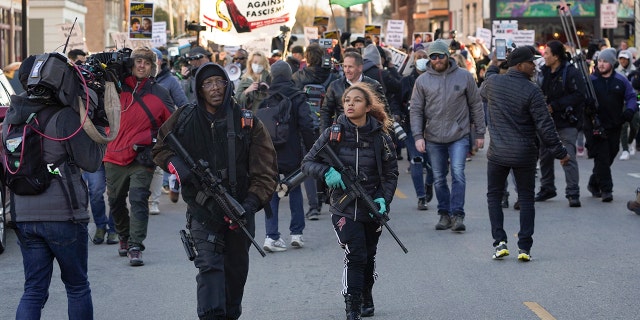 Erick Jordan and his daughter Jade, 16, carry rifles ahead of protesters marching, Sunday, Nov. 21, 2021, in Kenosha, Wis. (AP Photo/Paul Sancya)