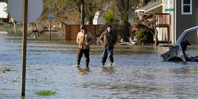 People walk through floodwaters Wednesday, Nov. 17, 2021, in Sumas, Washington.