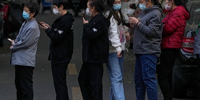 A woman walks through a line of masked service sector women waiting to receive a swab for a COVID-19 test during a mass testing in Beijing on Oct. 29, 2021, following a spike of the coronavirus in the capital and other provincials. 