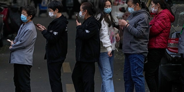 A woman walks through a line of masked service sector women waiting to receive a swab for a COVID-19 test during a mass testing in Beijing on Oct. 29, 2021, following a spike of the coronavirus in the capital and other provincials. 