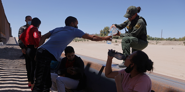 U.S. Border Patrol officer gives water to detained migrants waiting to be transported by the U.S. Border Patrol after crossing into the United States from Mexico in Andrade, California, U.S., April 19, 2021.
